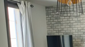 A dining area with a brick wall, a mounted TV, and a potted plant. - Cosy apartment, right in the center, 200m from the port  (La Ciotat)