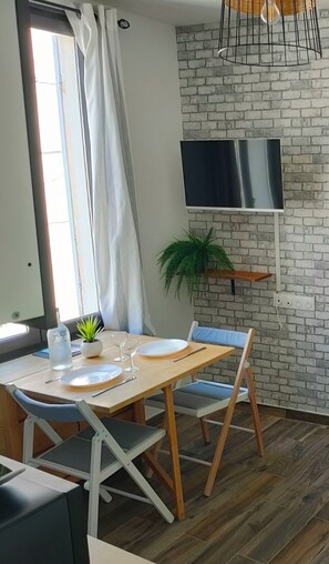 Comedor con pared de ladrillo, televisor montado y planta en maceta.