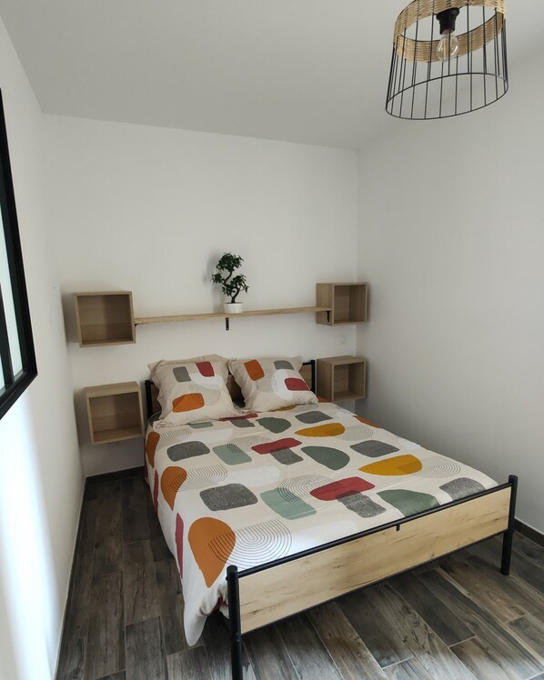 A bedroom with a bed, wooden headboard, bedside tables, a hanging light fixture, and a small potted plant. - Cosy apartment, right in the center, 200m from the port  (La Ciotat)