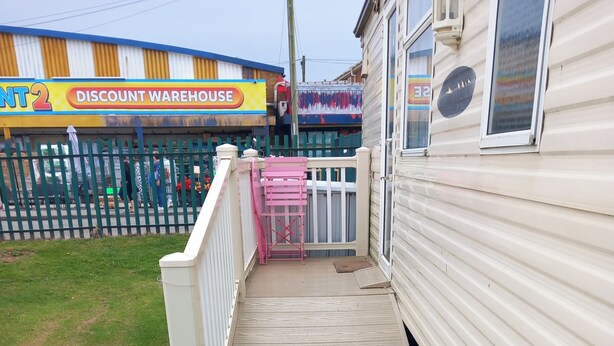 A wooden deck leading to a house with a gated entrance and a visible discount warehouse sign in the background. - Chapel St Leonards Happydays Beachfield (Skegness)