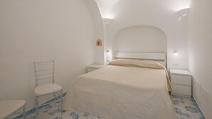 Une chambre à coucher comprenant un lit, une table de chevet, une chaise et une petite étagère fixée au mur.