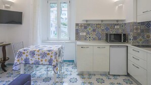 Une cuisine de taille réduite, dotée d’une fenêtre, d’un four à micro-ondes et d’une table recouverte d’une nappe à motifs.