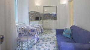 Une cuisine compacte avec un crédence carrelée, un coin repas avec une table et des chaises, et un canapé bleu agrémenté d’un coussin à motifs.