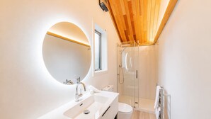 Ein modernes Badezimmer mit einem Doppelwaschbecken, einem runden Spiegel, einer Duschkabine aus Glas und einer Holzbalkendecke.