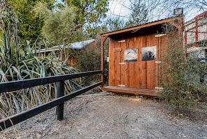 Eine hölzerne Hütte mit einem schwarzen Metallzaun davor, umgeben von Vegetation.