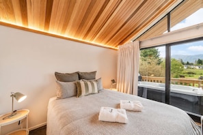 Ein Hotelzimmer mit einem großen Bett, einem Nachttisch, einer Lampe und Blick ins Freie.
