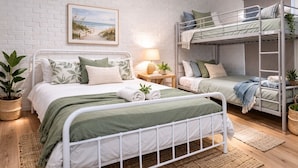 Een slaapkamer met stapelbed, een witte baksteenmuur, een ingelijst foto, een nachtkastje met lamp en een potplant.