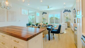 A modern kitchen with a wooden island, white cabinetry, and a dining area with a table and chairs. - SunKissed @ St. George Island (Eastpoint)