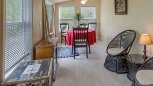 Un coin repas avec une table dressée pour deux personnes, un ventilateur de plafond et une fenêtre avec des stores.