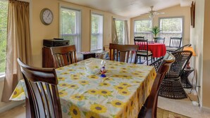 Un coin repas avec une table recouverte d’une nappe à motifs de tournesols, entourée de chaises en bois.