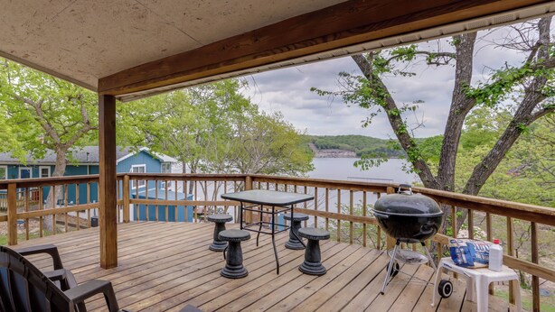 Une terrasse en bois avec une table et des chaises, un barbecue et une vue sur un lac et des arbres.