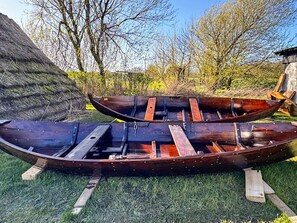 Two wooden boats on grass with a tree and a building in the background.