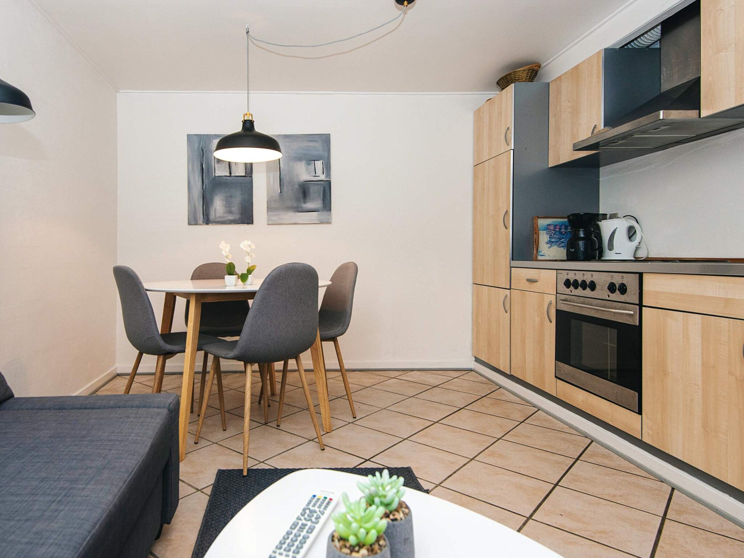 Una cocina compacta con armarios de madera, un comedor con mesa y sillas, y una lámpara colgante.