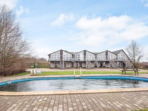 A building with a swimming pool, a covered patio, and a staircase leading to an upper level.