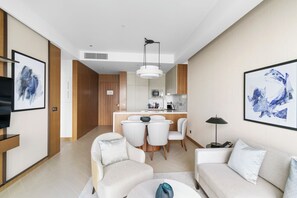 A modern living room with a sofa, chairs, and a dining area. There is a kitchen in the background with a microwave and cabinets.