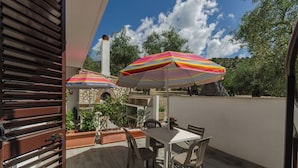 Eine Terrasse im Freien mit Tisch und Stühlen, zwei gestreiften Sonnenschirmen und einem Kamin aus Stein.