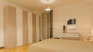 Ein Schlafzimmer mit einem großen Bett, einem Kleiderschrank, einem Spiegel und einem Nachttisch mit einer Lampe.