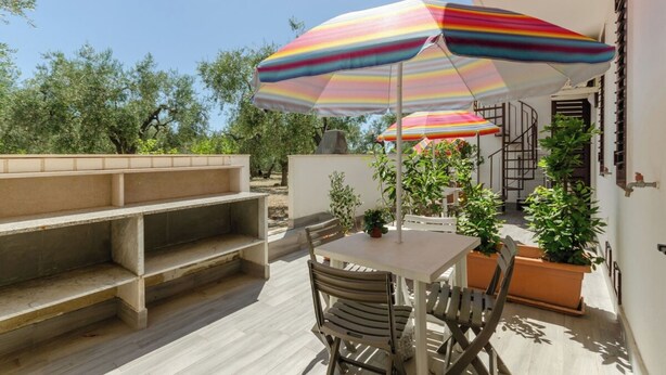 Un patio al aire libre con una mesa, sillas, sombrillas a rayas y plantas en macetas.