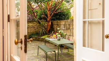 Un patio con una mesa lista para comer, rodeado por un muro de piedra y un árbol.