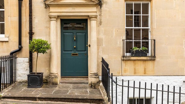 A traditional building with a green door, a small balcony with plants, and a stone staircase leading to the entrance. - Grand Georgian Townhouse With Garden (Bath)