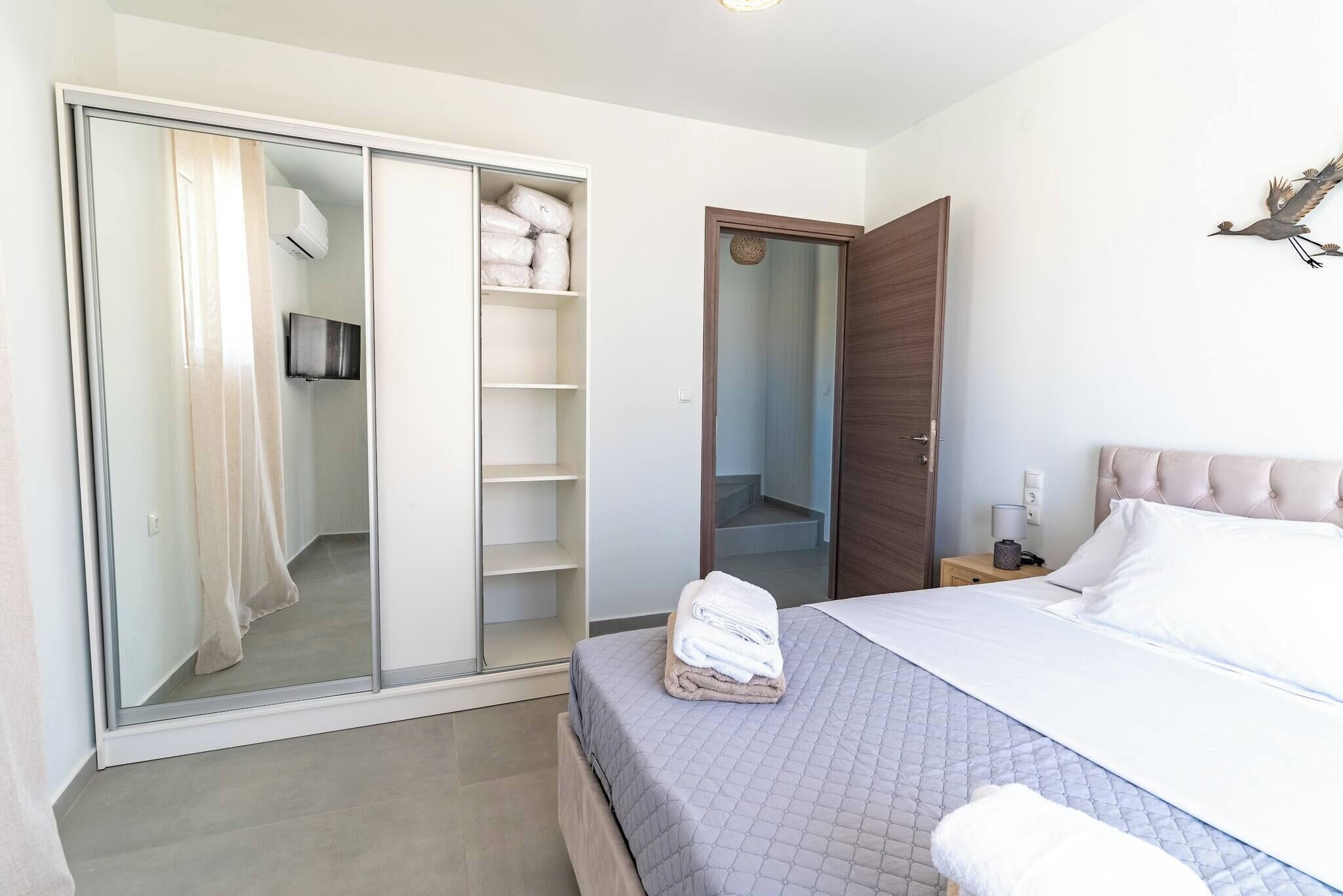 Un dormitorio con cama, armario, espejo y mesita de noche.