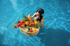 A poolside scene with a wicker basket filled with fruits and flowers.