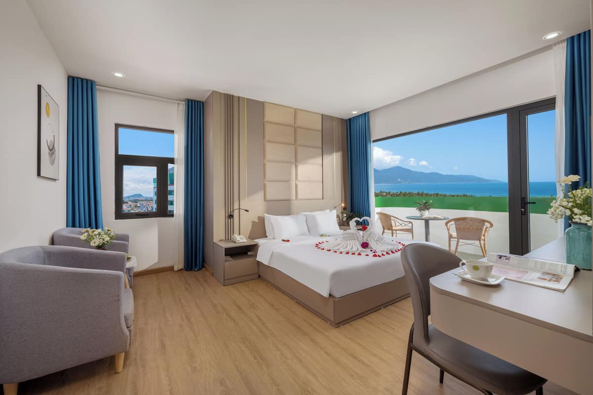 Habitación de hotel con una cama, dos sillas, un escritorio y vista al mar.