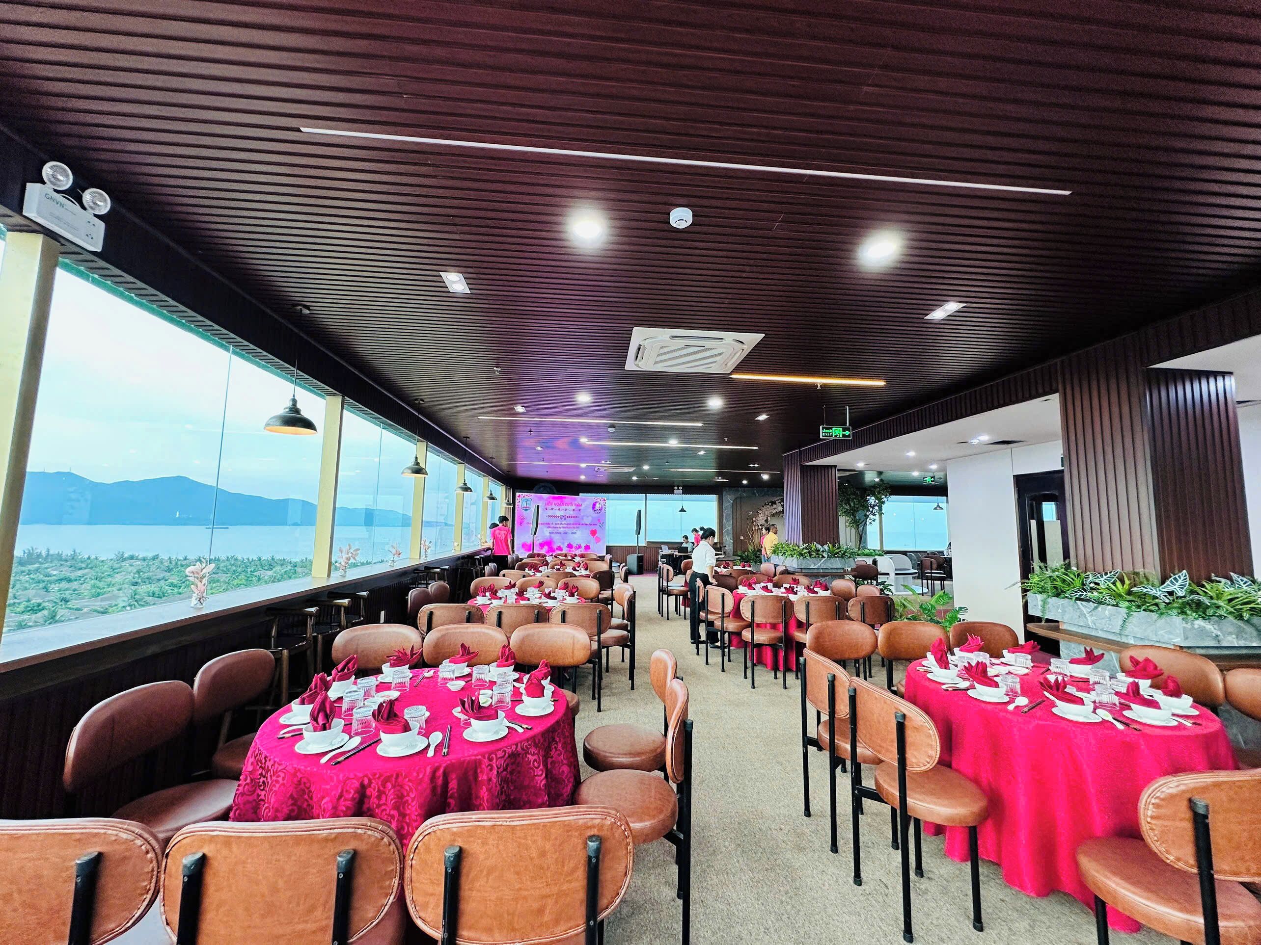 A spacious indoor dining area with multiple round tables set for dining, featuring red tablecloths and white tableware.