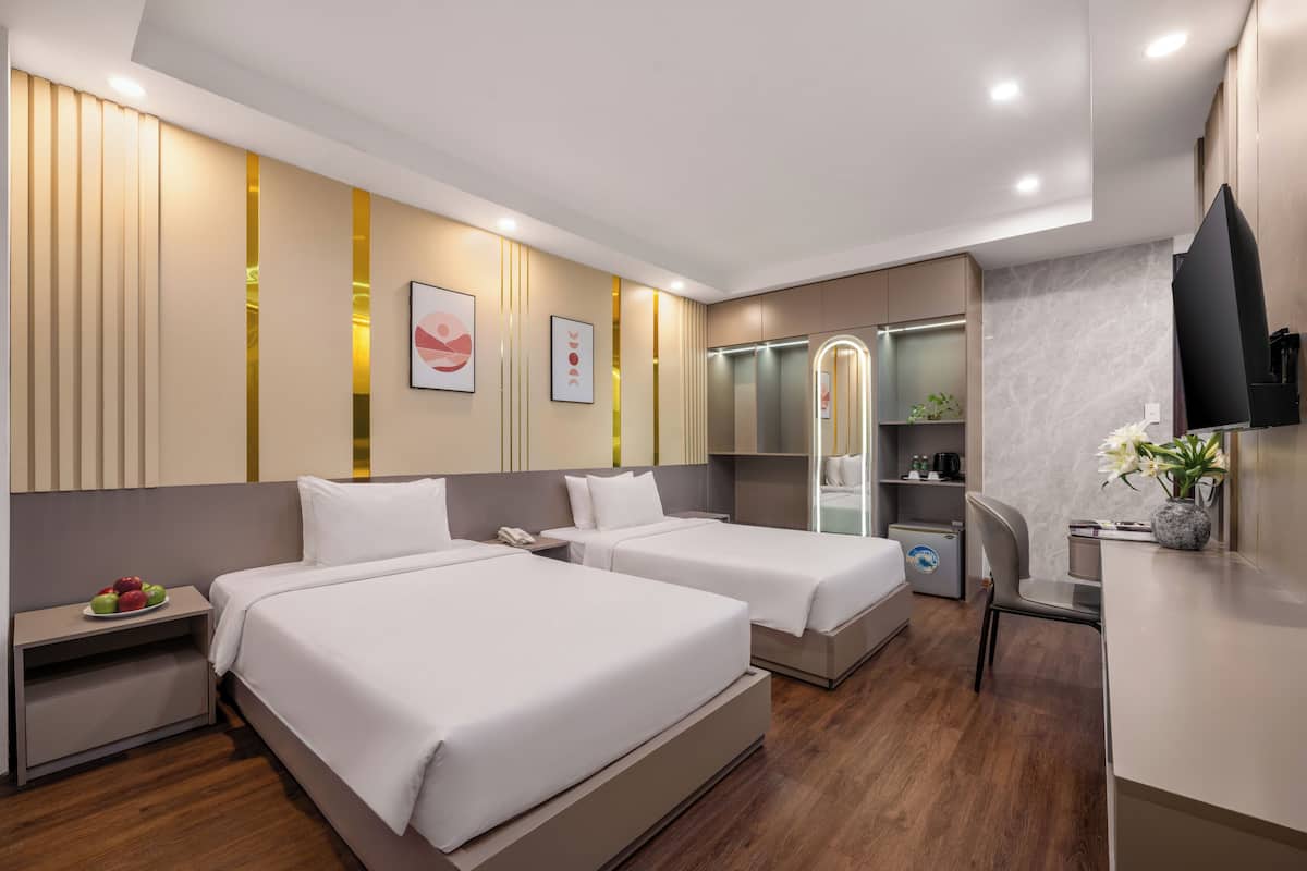 Habitación de hotel con dos camas, un escritorio, una silla, un televisor, un minibar y un baño con espejo e inodoro.