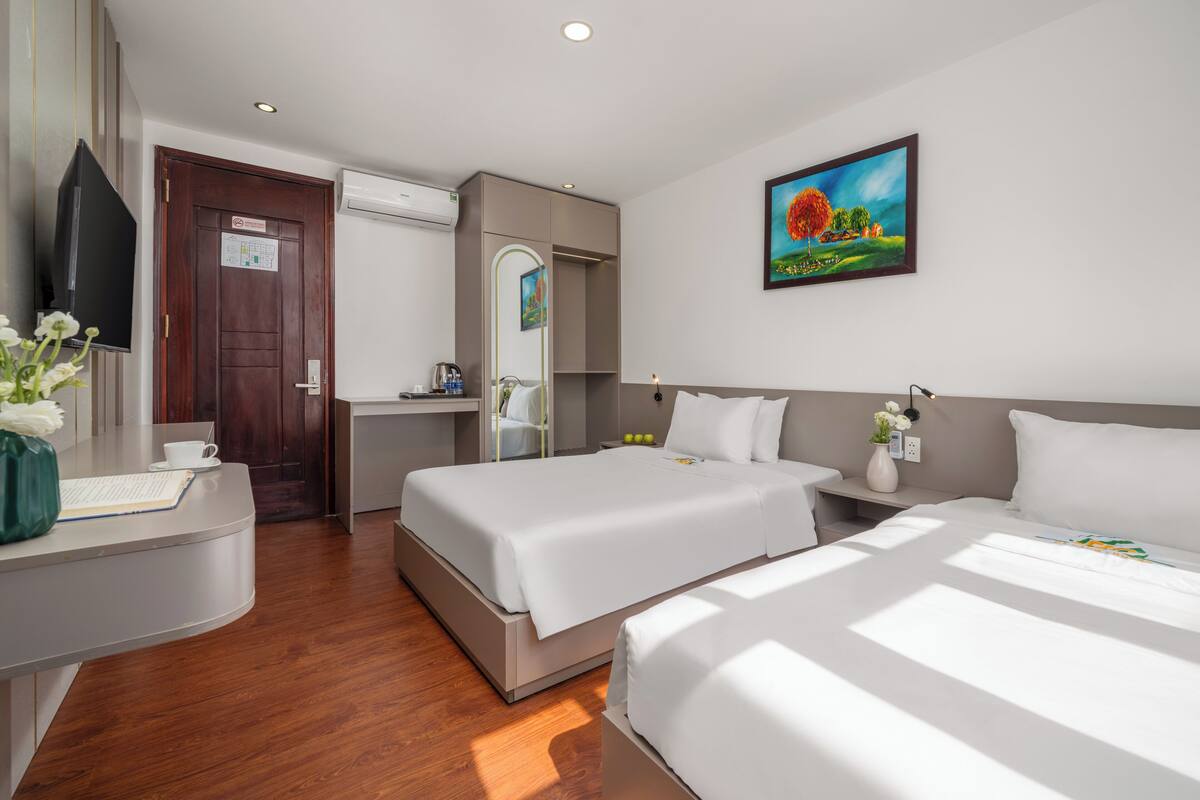Habitación de hotel con dos camas, un escritorio con computadora, un televisor y un cuadro en la pared.