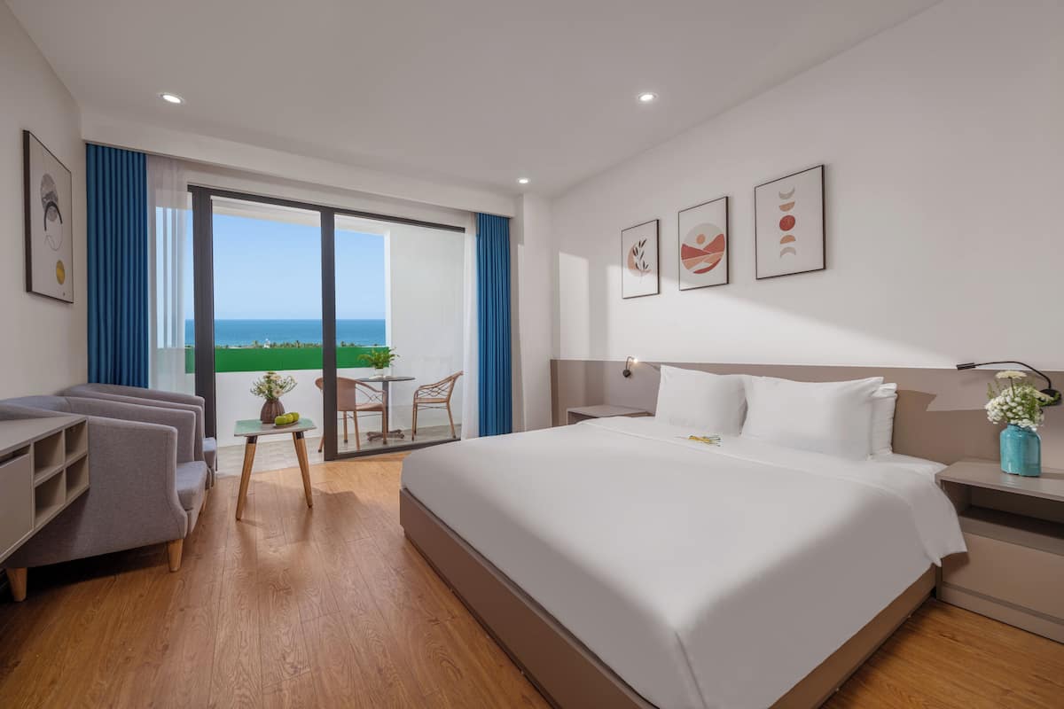 Habitación de hotel moderna con una cama grande, un escritorio, una silla y un balcón con vista al mar.