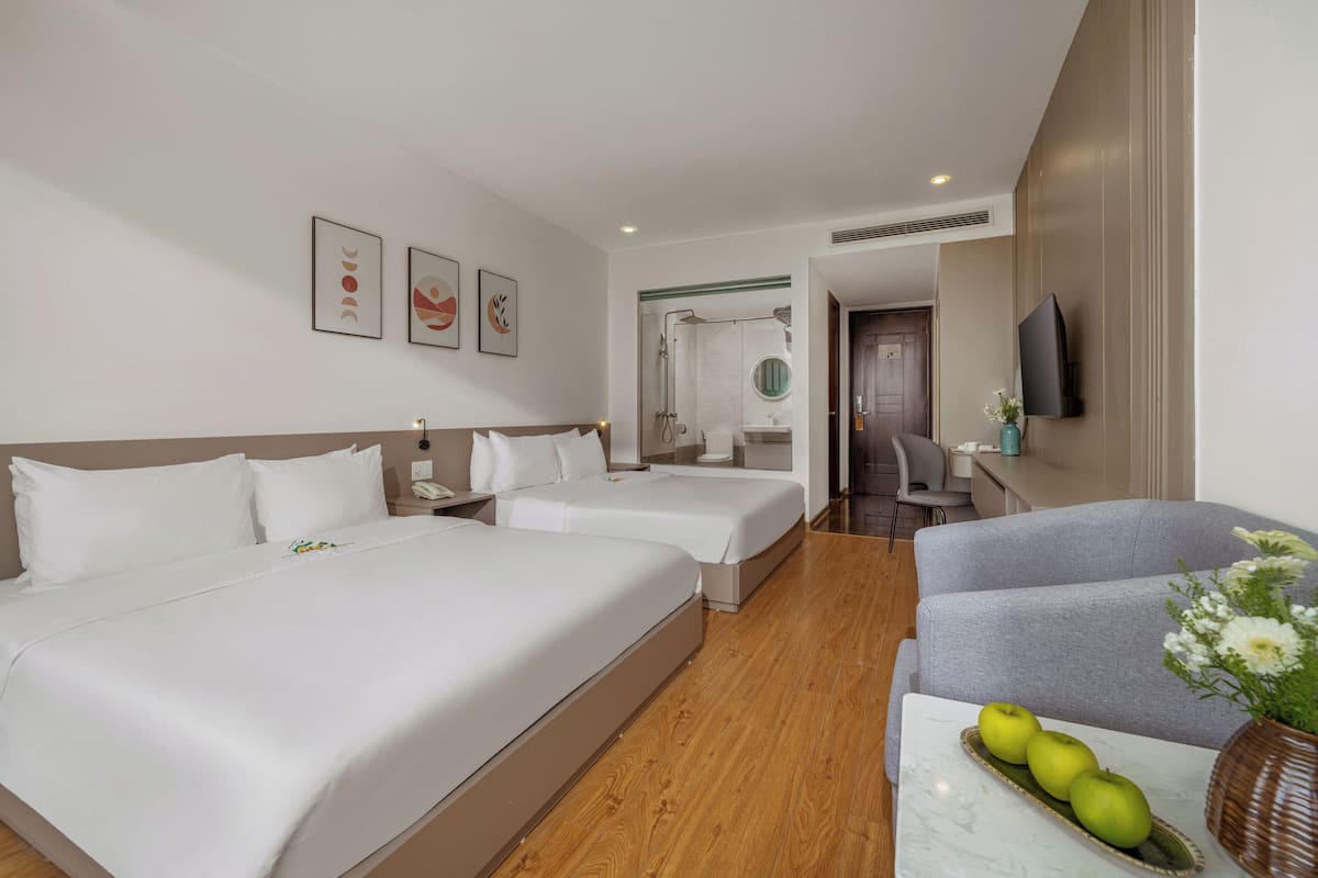 Habitación de hotel con dos camas, un sofá, una mesa con manzanas y flores, un televisor y obras de arte en la pared.