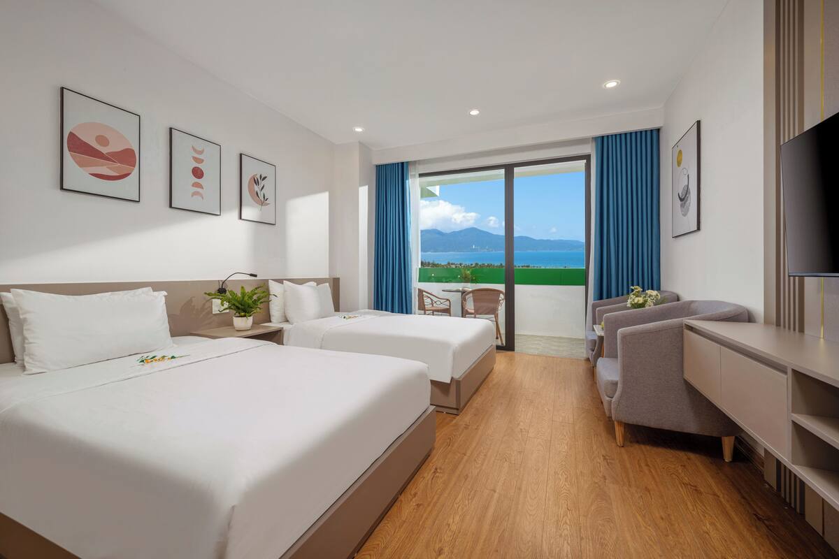 Habitación de hotel con dos camas, un escritorio, un televisor y un balcón con vista al mar.