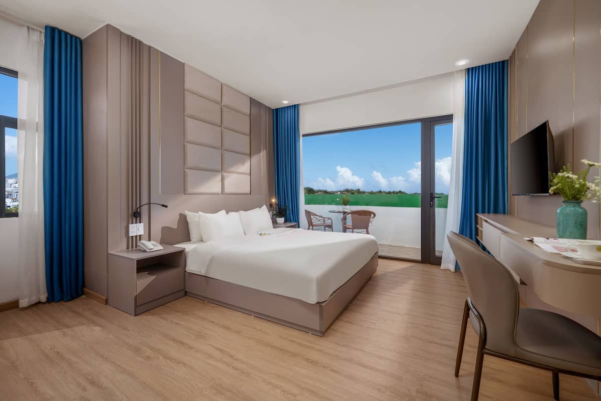 Habitación de hotel moderna con una cama grande, un escritorio y vistas a un paisaje verde.