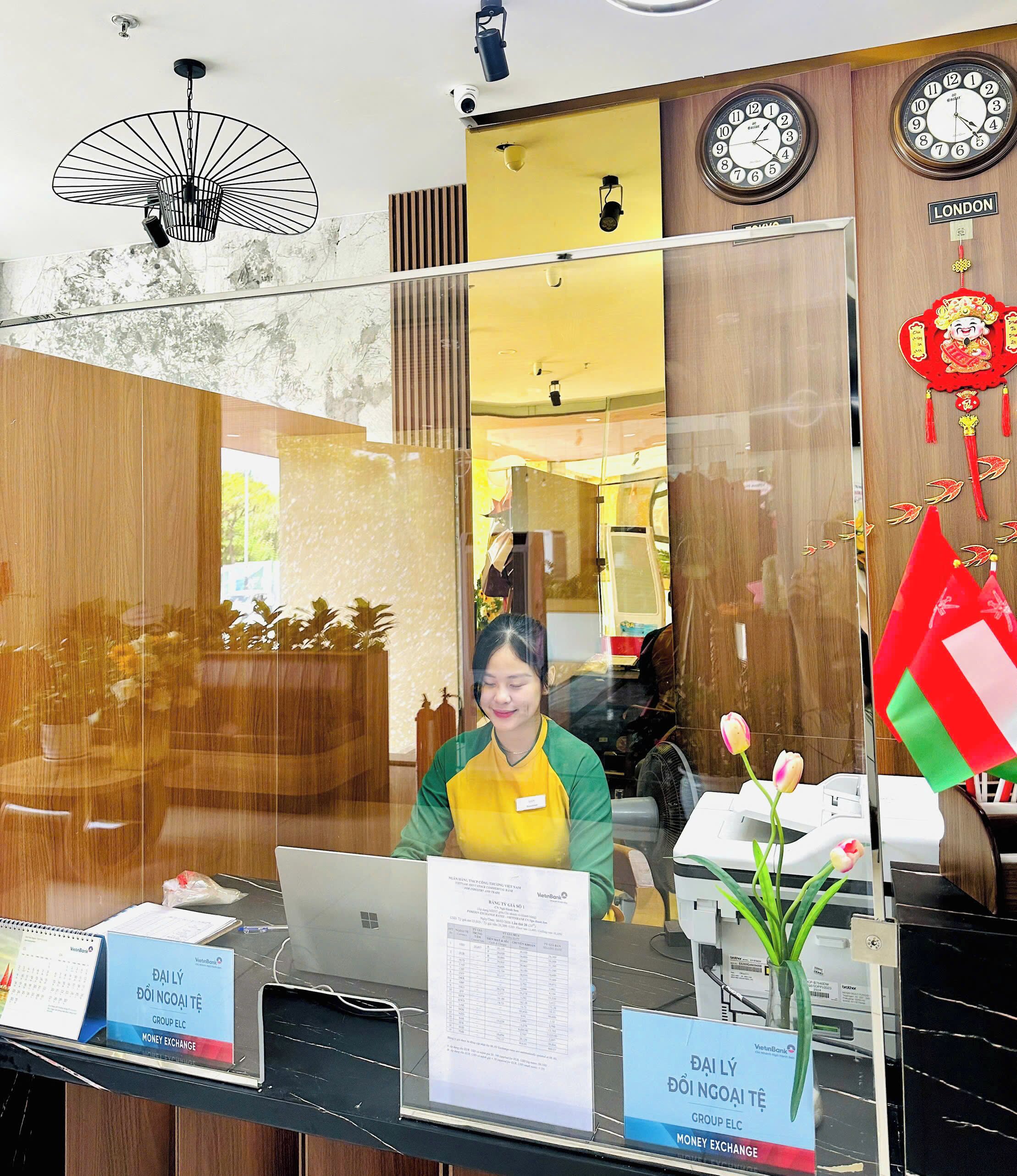A reception desk with a laptop, a vase with flowers, and a clock on the wall.