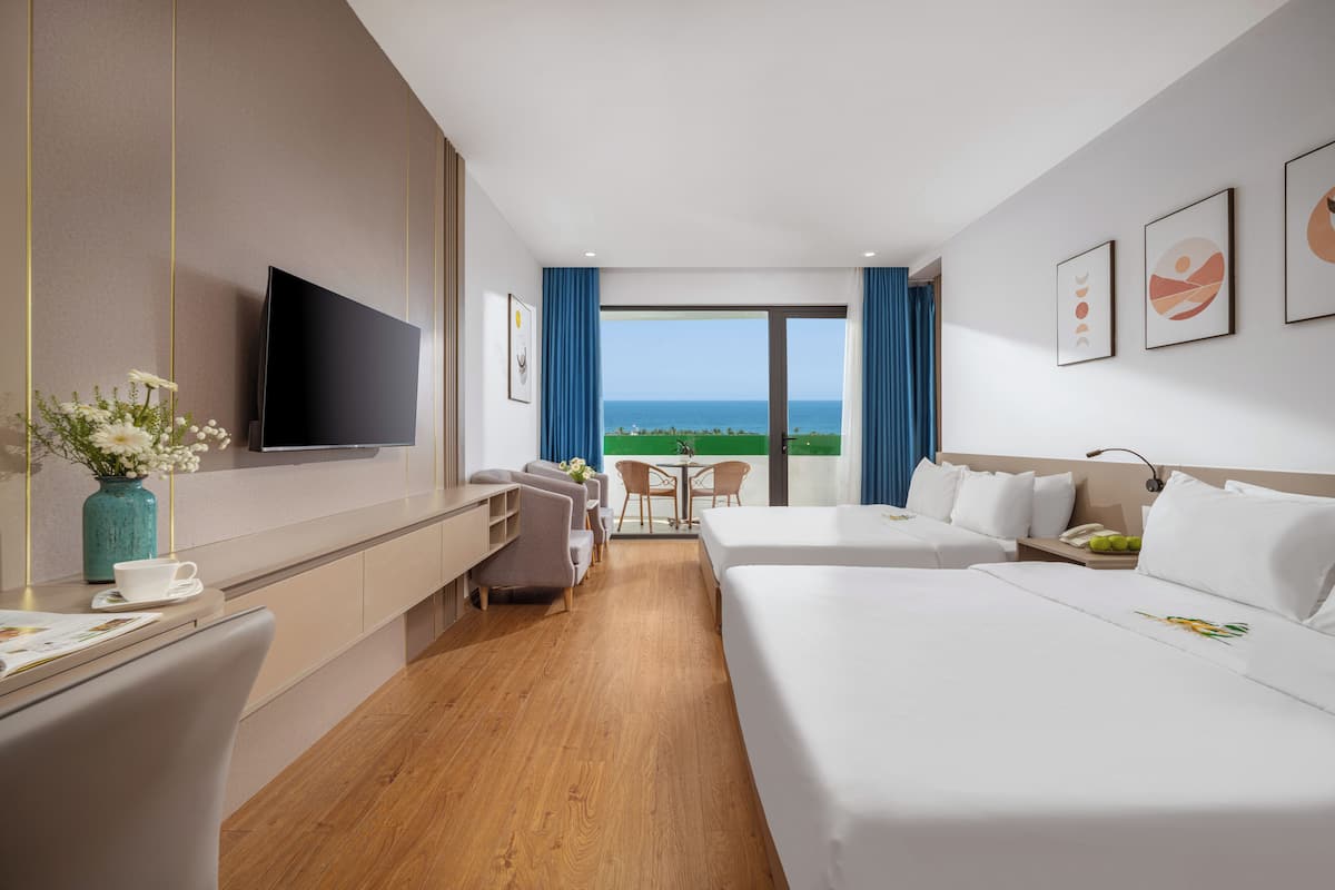 Habitación de hotel con televisión, dos camas, escritorio, silla, una mesita y vistas al océano.