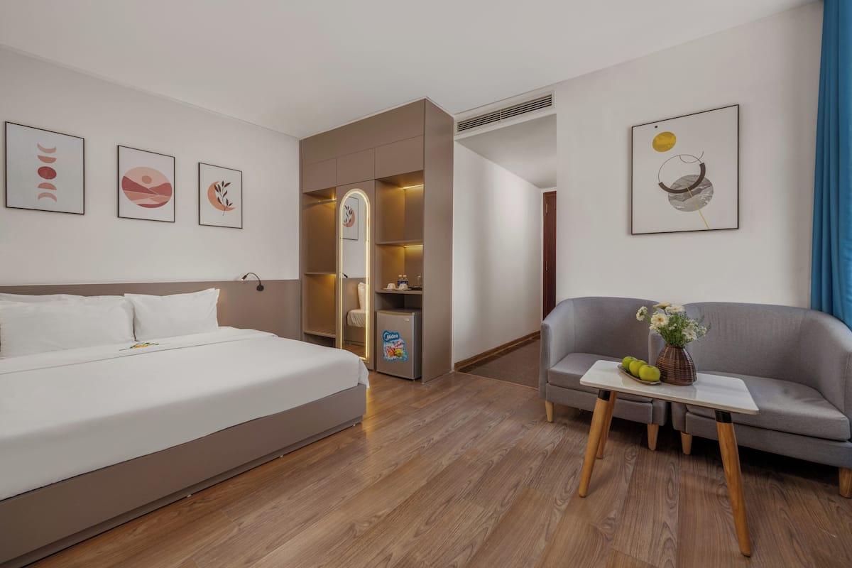 Una habitación de hotel moderna con una cama, un sofá gris, una mesita con un jarrón y manzanas, y obras de arte en las paredes.