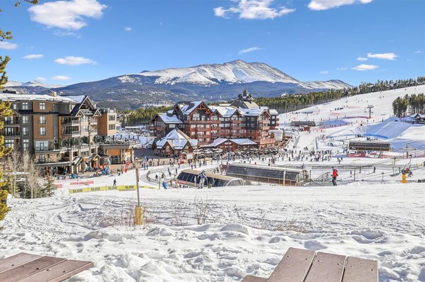A ski resort with a mountain backdrop, featuring a mix of traditional and modern buildings, ski lifts, and a well-maintained snow-covered slope.
