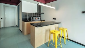 A compact kitchen with a central island, two yellow stools, a microwave, and a coffee maker. - Super Stylish Apartment by Wehost (Kazbegi)