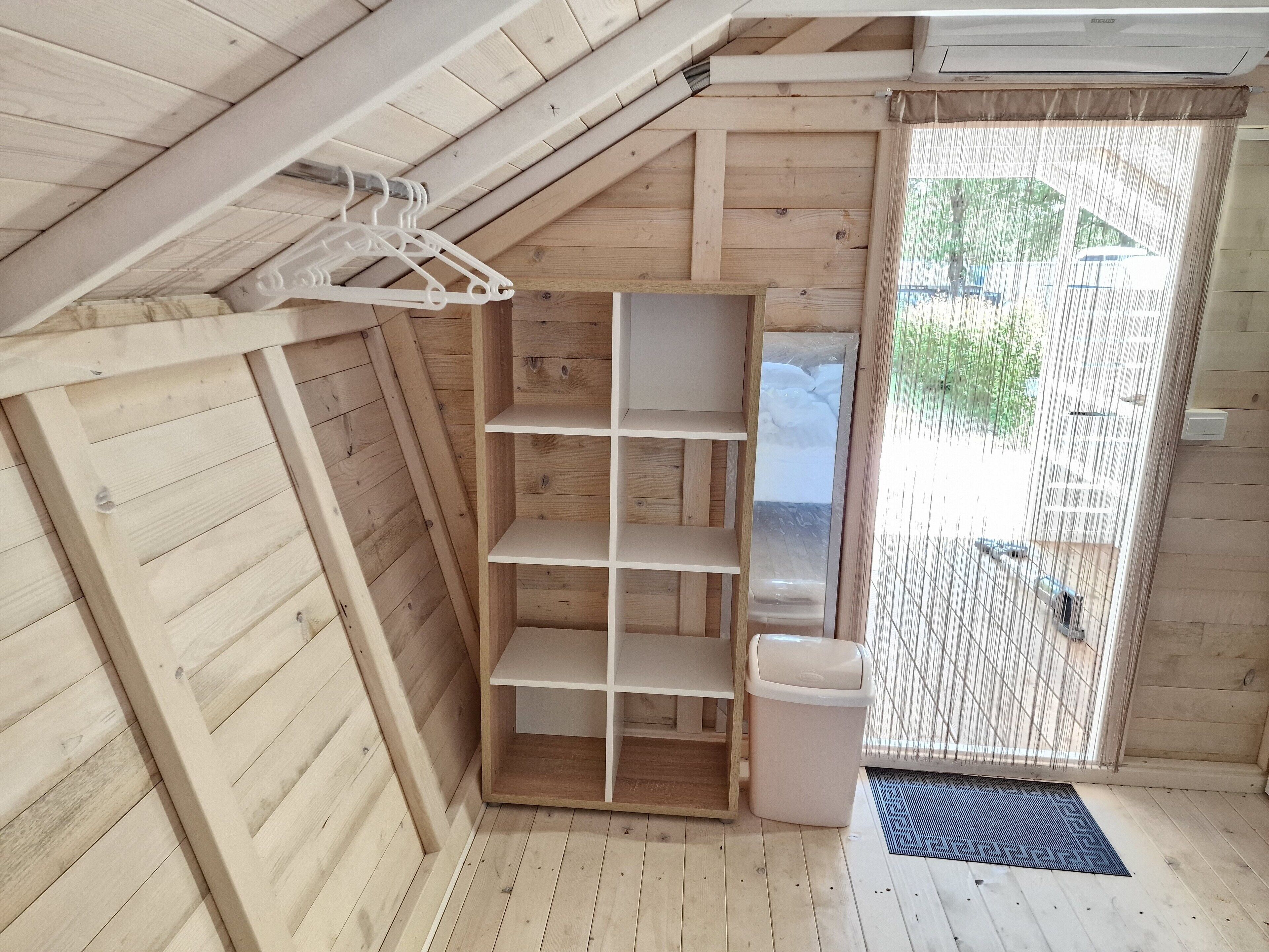 A wooden attic room with a built-in shelf unit, a waste bin, and a door leading outside.