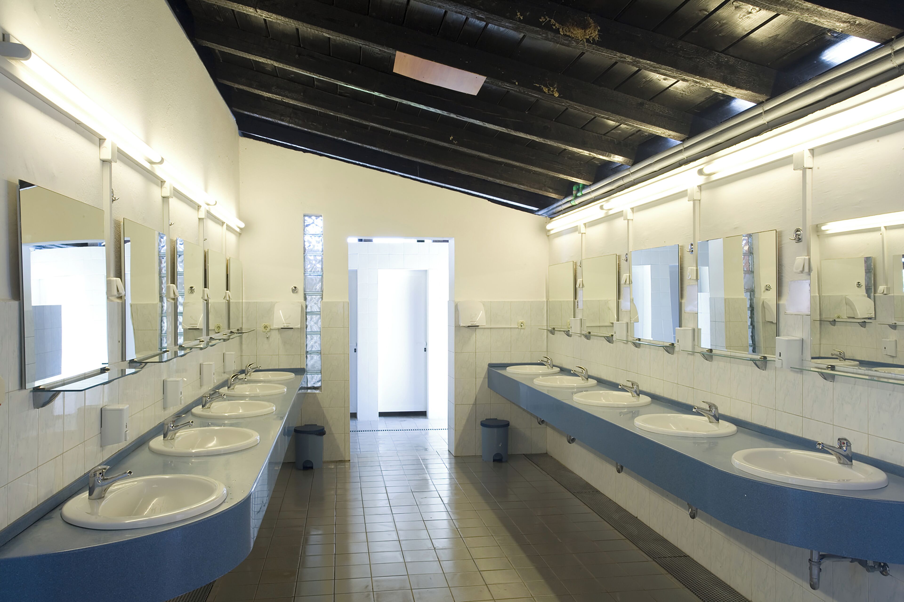 A public restroom with multiple sinks and mirrors, a tiled floor, and a door leading to another room.