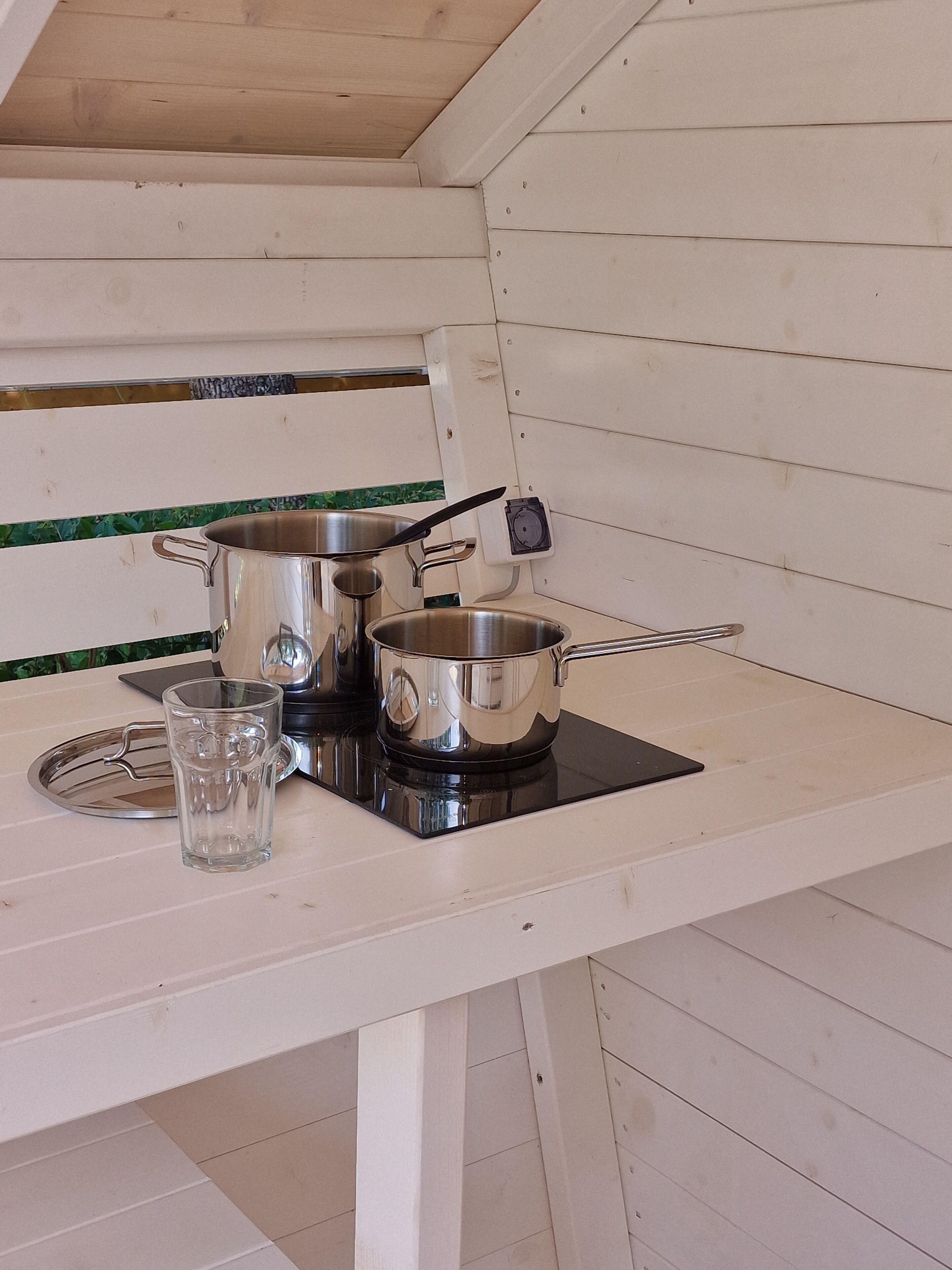 A kitchenette with a stove, pots, and a glass.