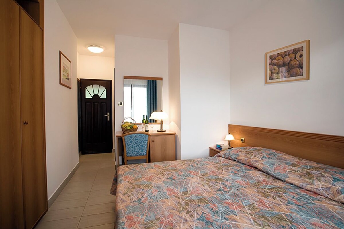 Une chambre d’hôtel avec un lit, un bureau doté d’une lampe, une chaise et une porte donnant sur une autre pièce.