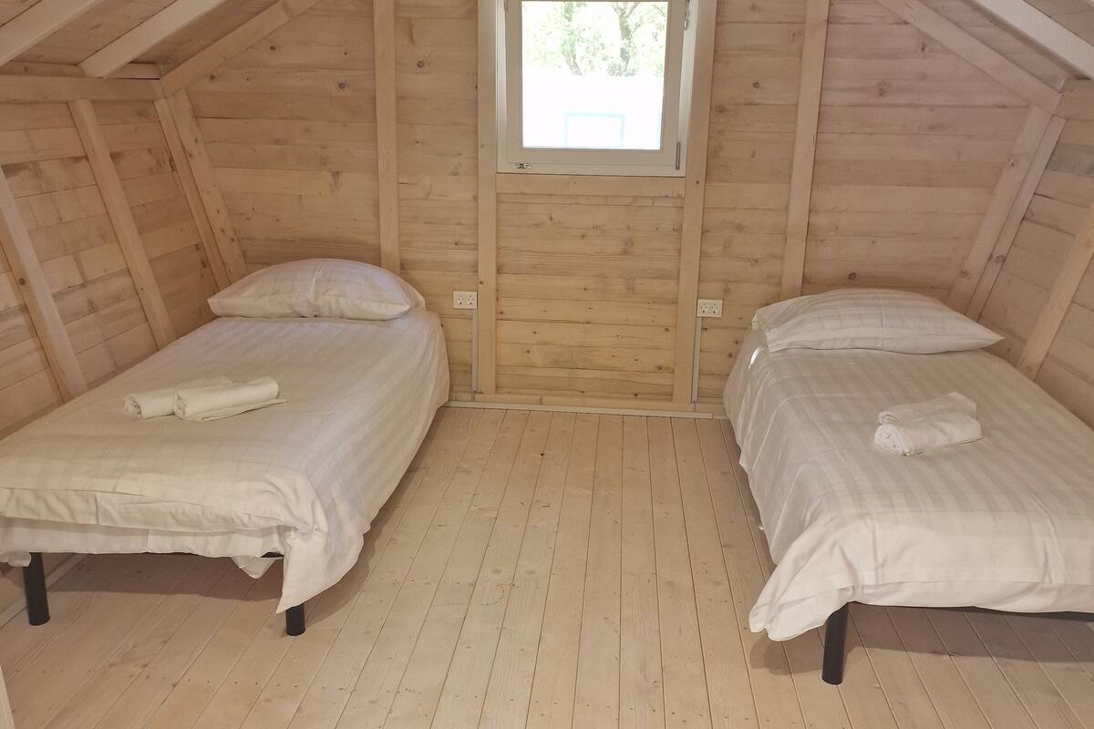 Een kleine zolderkamer met twee bedden, houten wanden, een raam en een schuine plafond.