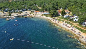 Vue aérienne d’une zone côtière avec une plage, des bateaux et un port de plaisance.