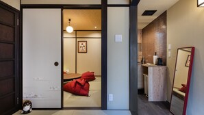 A traditional Japanese room with tatami flooring, a low wooden table, and red cushions. - Shiki Homes MEIGETSU (Kyoto)