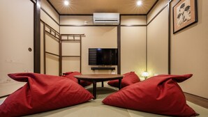 A room with tatami flooring, a tatami mat table, red cushions, a television, and an air conditioning unit. - Shiki Homes MEIGETSU (Kyoto)
