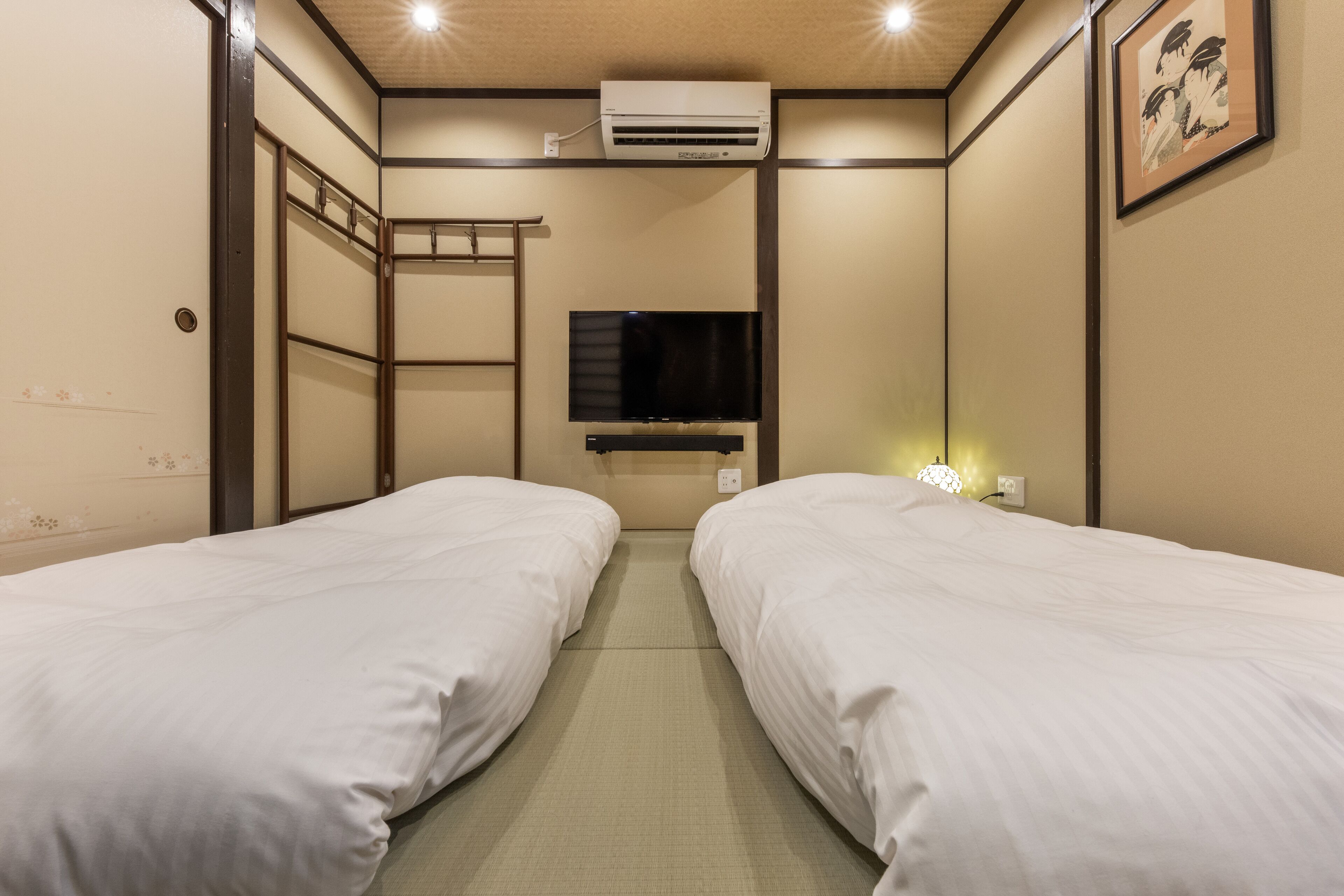 A hotel room with two single beds, a TV mounted on the wall, an air conditioning unit, and a ladder against the wall.