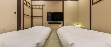A hotel room with two single beds, a TV mounted on the wall, an air conditioning unit, and a ladder against the wall.