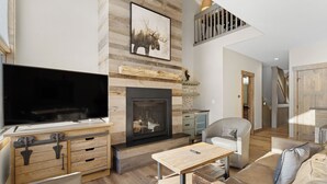 Uma sala de estar moderna com lareira, televisão de tela plana, móveis de madeira e escada para um andar superior.